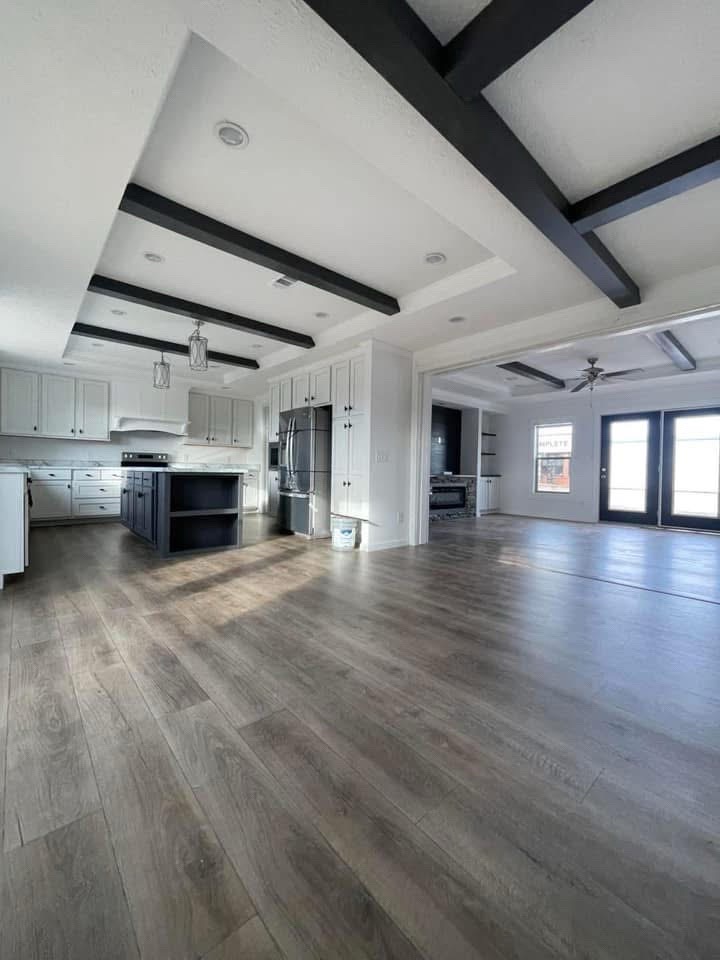 Spacious modern kitchen with hardwood floors, white cabinets, a dark central island, and stainless steel appliances. Ceiling beams add contrast and elegance.