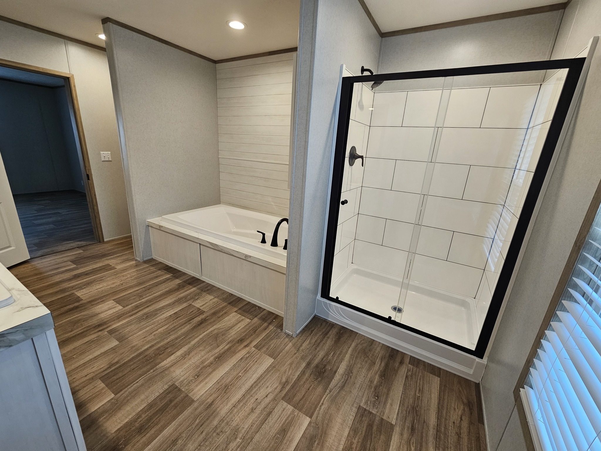 Modern bathroom with a glass shower enclosure and a separate built-in bathtub. The room features wood-patterned flooring and white tiled walls, creating a clean, contemporary look.