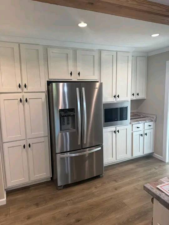 Modern kitchen with white cabinets, stainless steel fridge, and microwave. Light wood floor and neutral tones create a clean, inviting atmosphere.