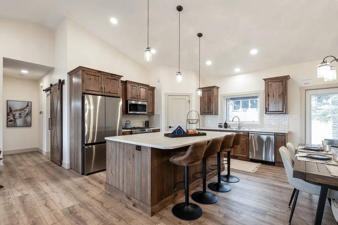 Spacious kitchen with rustic charm, featuring wooden cabinets, stainless steel appliances, and a large island with stools. Dining table set for four.