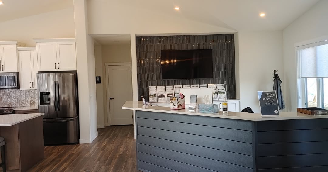Modern interior of a real estate office with a sleek reception desk, a wall-mounted TV, property brochures, and cozy kitchen area, conveying a welcoming and professional atmosphere.