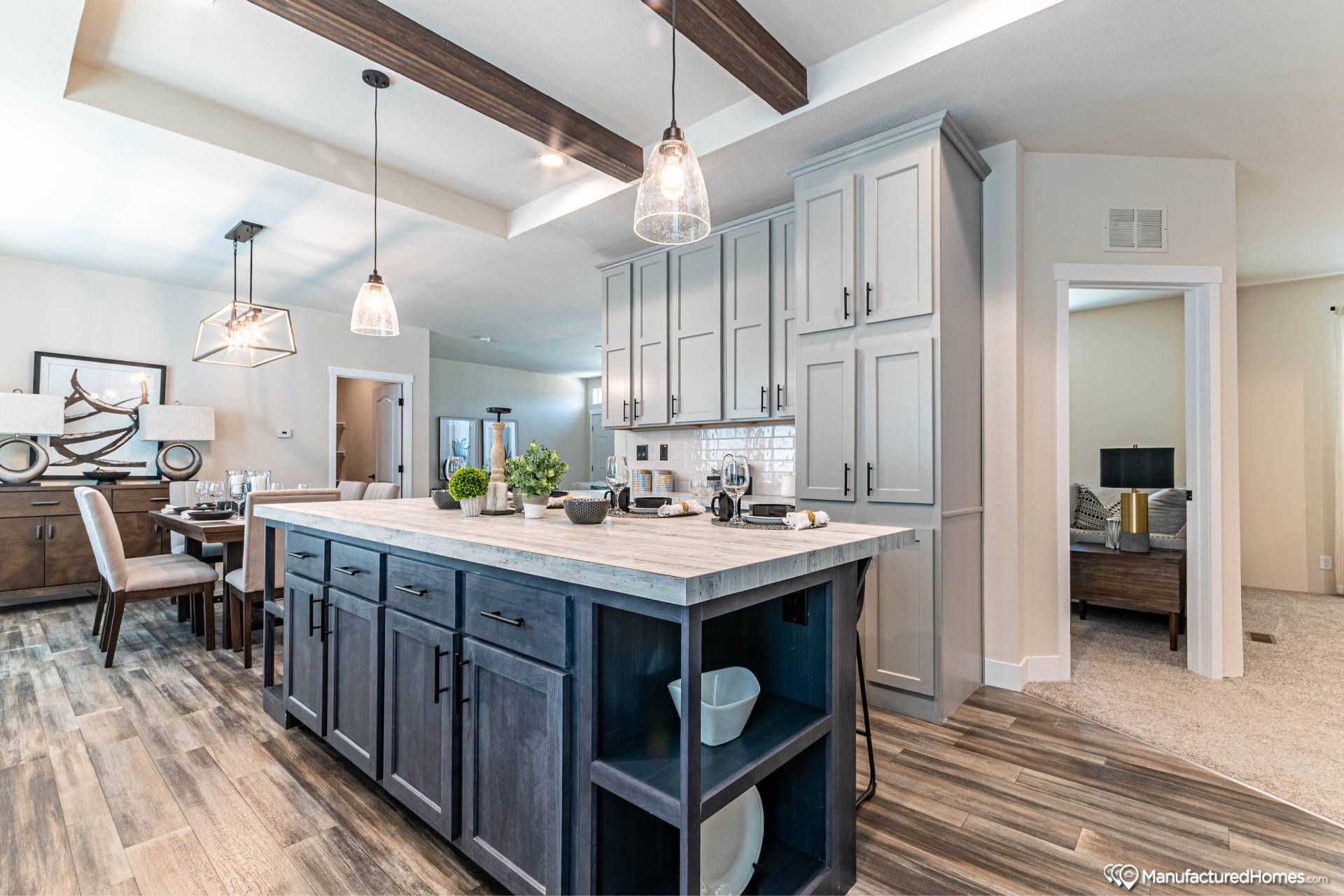 Modern kitchen with a wooden island, pendant lights, and gray cabinets. Open dining area on the left. Warm, contemporary ambiance with natural wood flooring.
