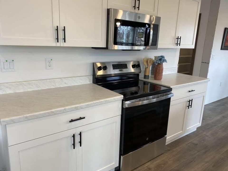 Modern kitchen with white cabinets, black handles, stainless steel stove and microwave. Light wood flooring adds a warm tone to the sleek design.