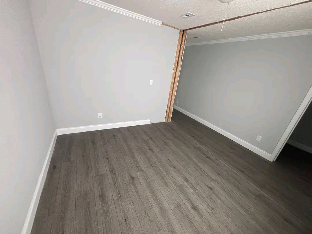 An empty room with gray walls, dark wood laminate flooring, and white baseboards. The room has a partial wall divider and a simple, modern look.