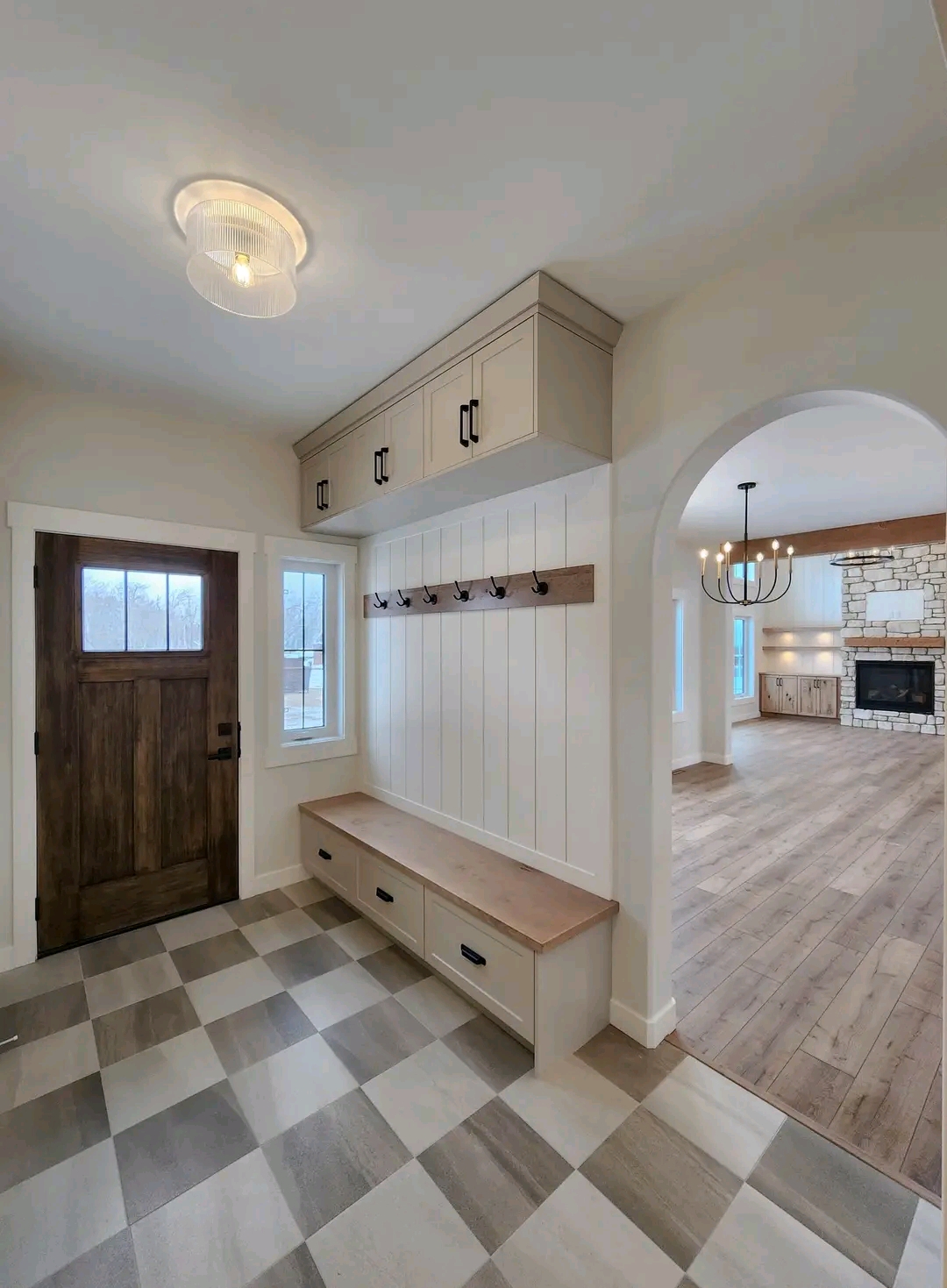 Inviting entryway with a wooden door, checkered tile floor, and a bench with storage. An arch leads to a cozy living room with a stone fireplace.