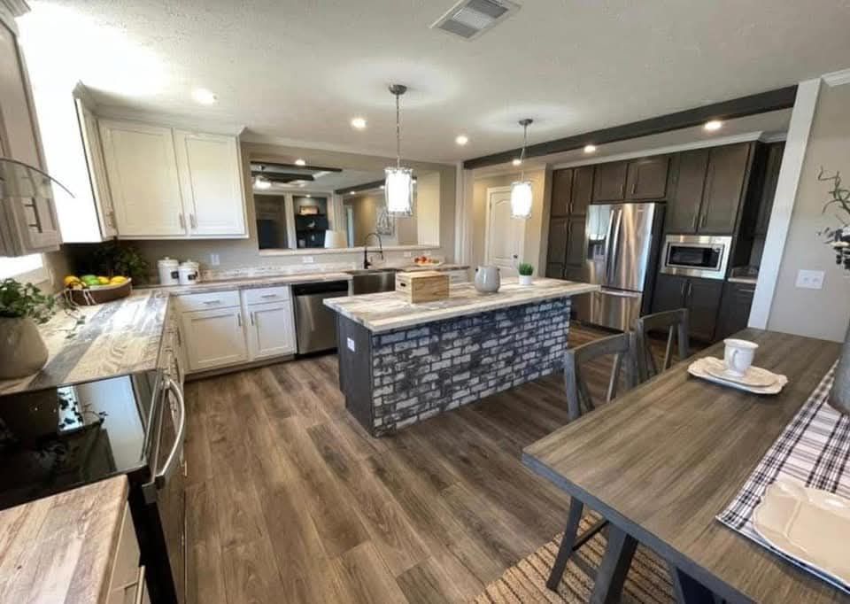 Modern kitchen with white and dark wood cabinets, stone island, and wooden floors. Pendant lights add a cozy feel; a dining table sits nearby.