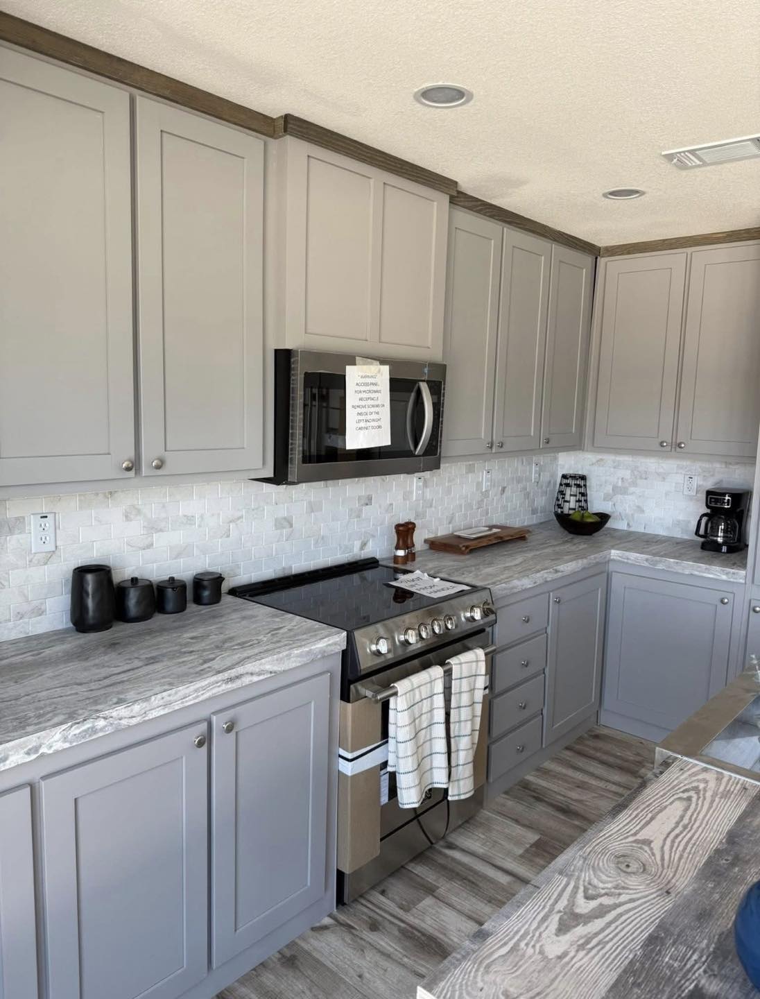 Modern kitchen with gray cabinets, marble countertops, and a sleek stainless-steel oven. A striped towel hangs from the oven door, adding a homely touch.