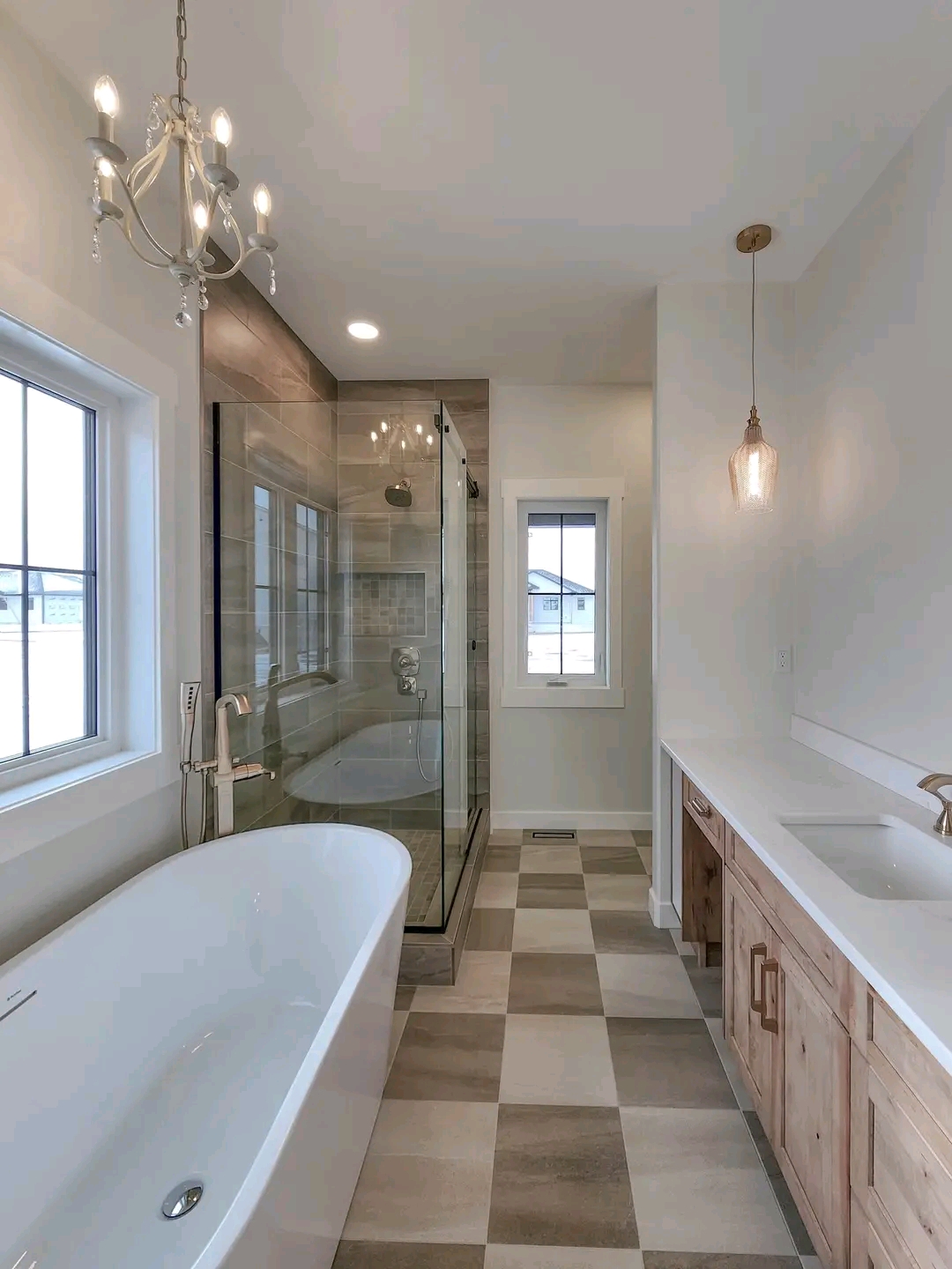 Modern bathroom with a freestanding bathtub, glass-enclosed shower, and wooden vanity. Checkered floor tiles and hanging lights add elegance. Calm ambiance.