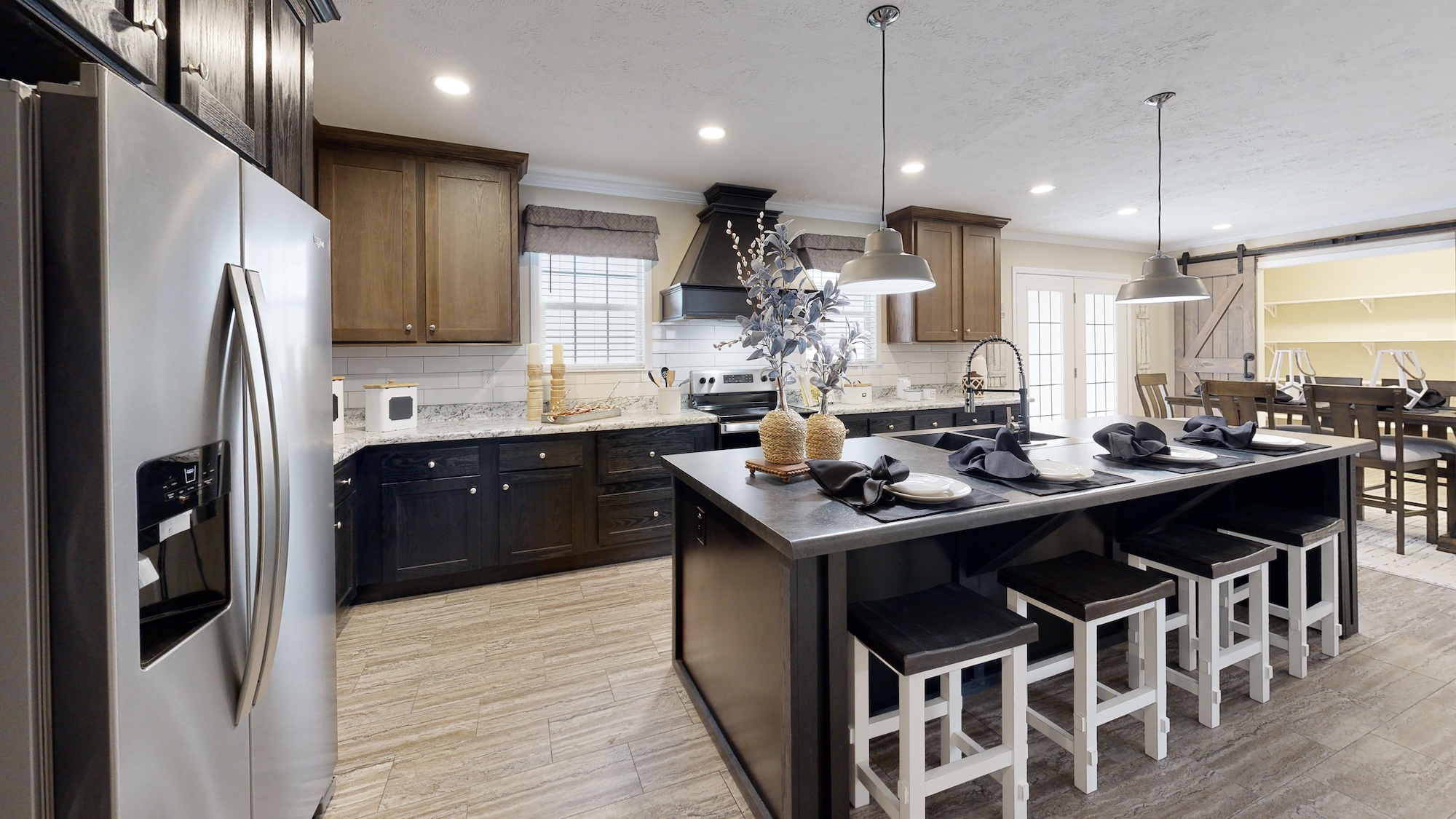 A modern kitchen with stainless steel appliances, dark wooden cabinets, and a large island with bar stools. Pendant lights add a warm ambiance.