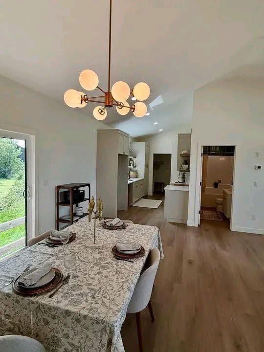 Dining room with a patterned tablecloth set for four, under a modern spherical chandelier. Open kitchen in the background, natural light through sliding doors.