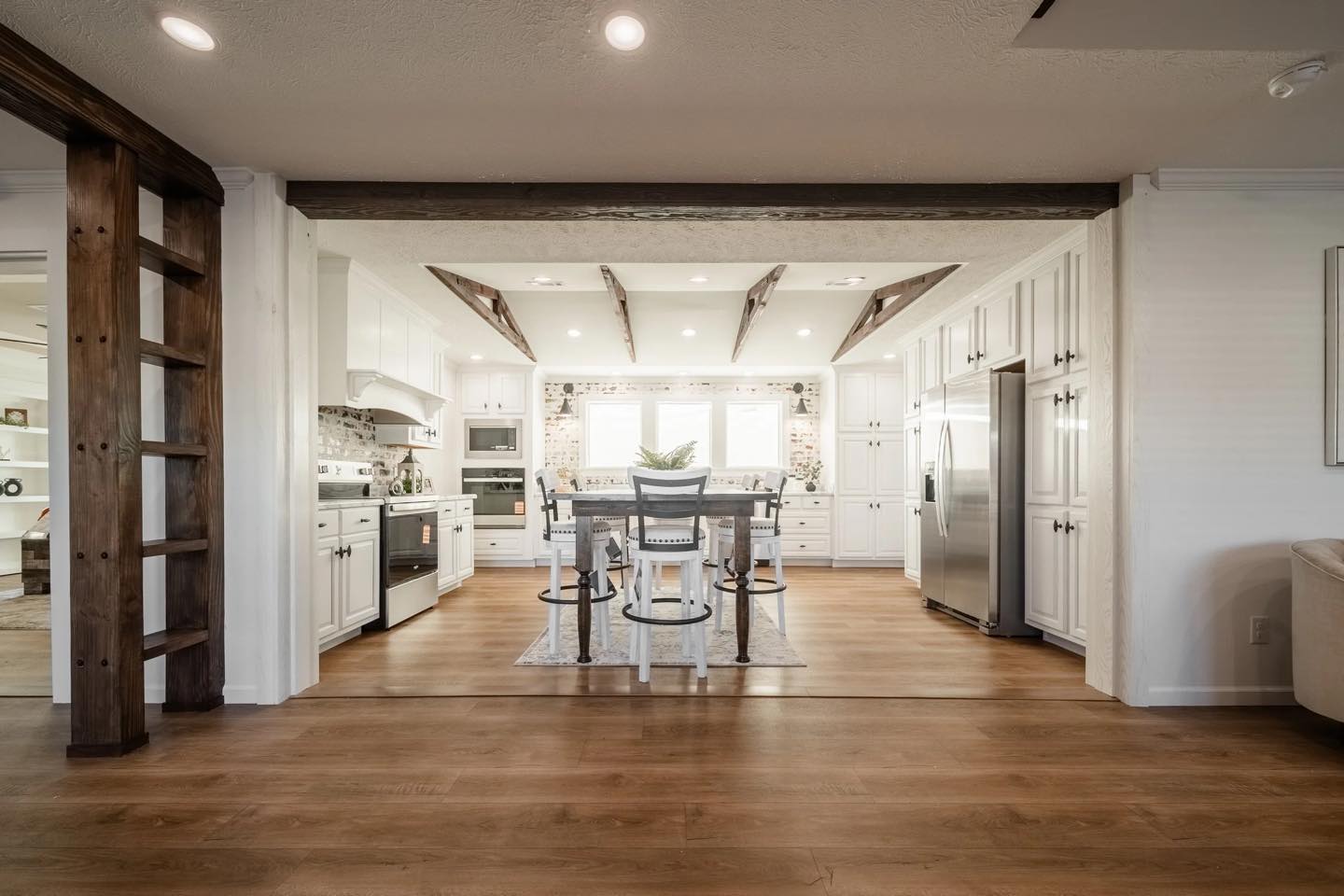 Spacious kitchen with white cabinetry, large island, and barstool seating. Exposed beams, stainless steel appliances, and bright, inviting atmosphere.