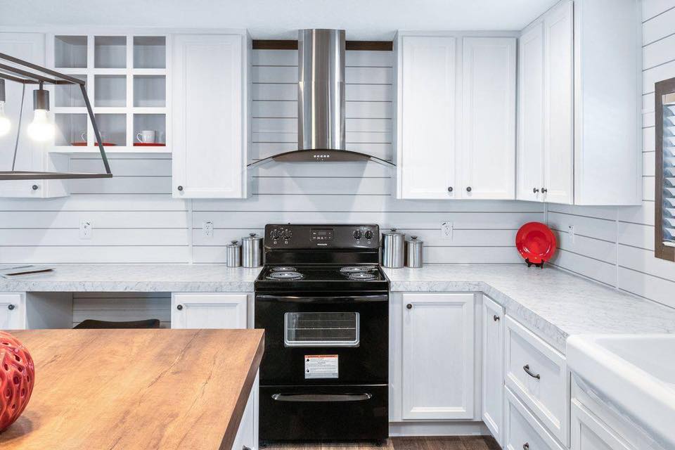 Modern kitchen with white cabinets and a black stove, featuring a wooden island in the foreground. A red fruit bowl adds a pop of color.