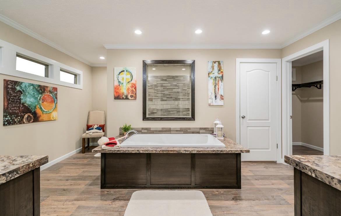 Modern bathroom with a central bathtub, beige walls, wooden floors, abstract art, and soft lighting. The atmosphere is warm and inviting.