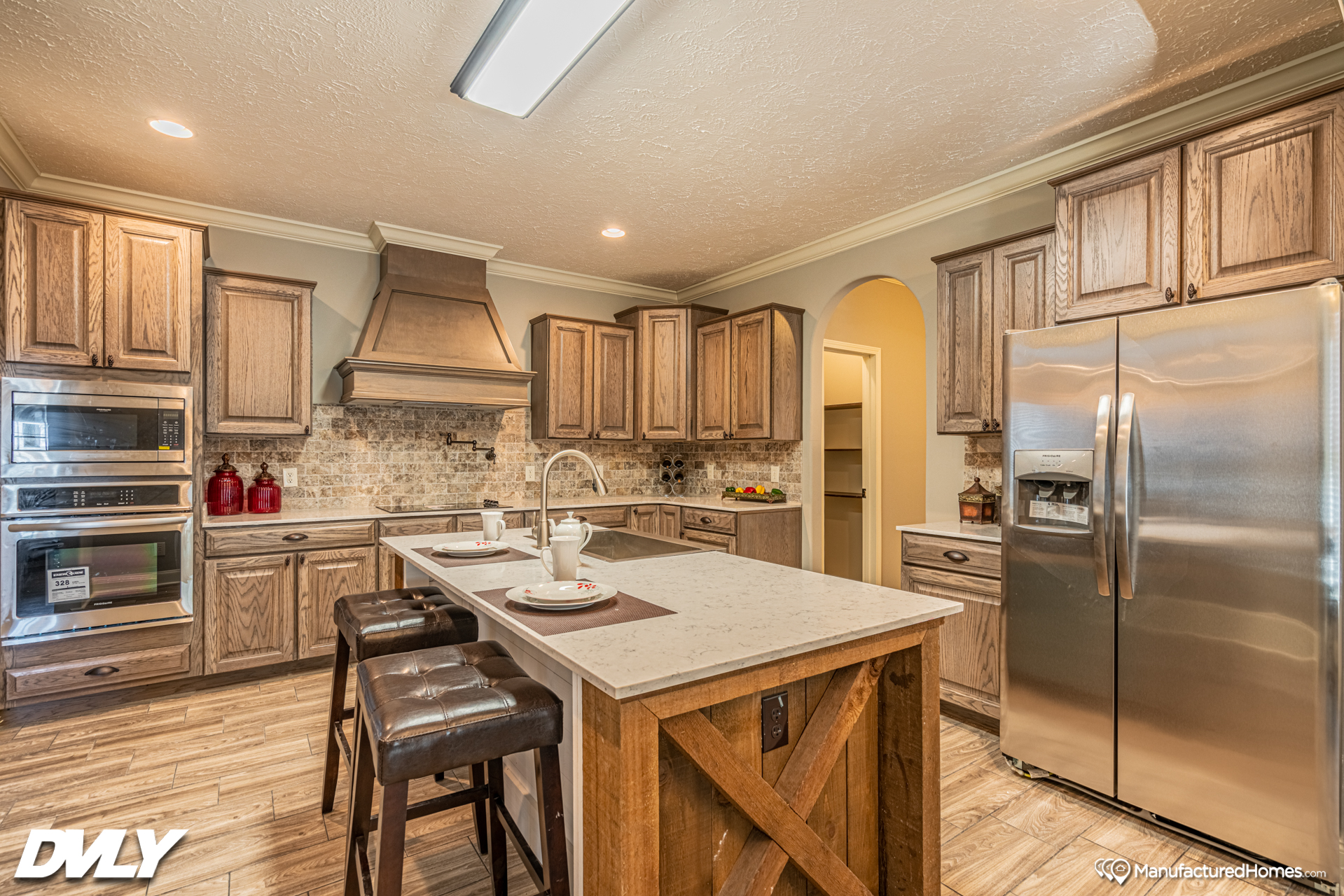 Warm, inviting kitchen with rustic wood cabinetry, stone backsplash, and a central island featuring leather stools. Stainless steel appliances add a modern touch.