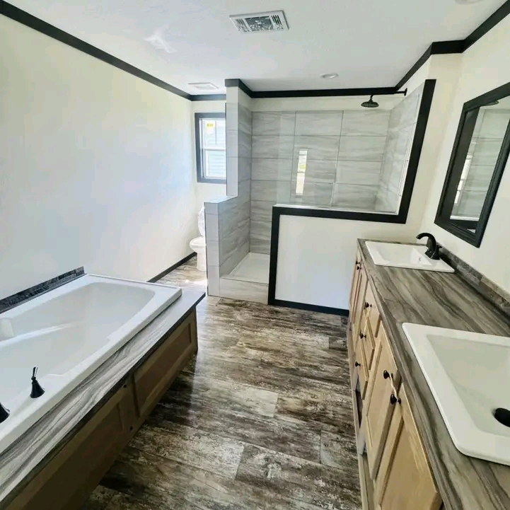 Modern bathroom with a rustic touch, featuring a wooden double vanity, large bathtub, and glass-enclosed shower. Natural light enhances the sleek design.