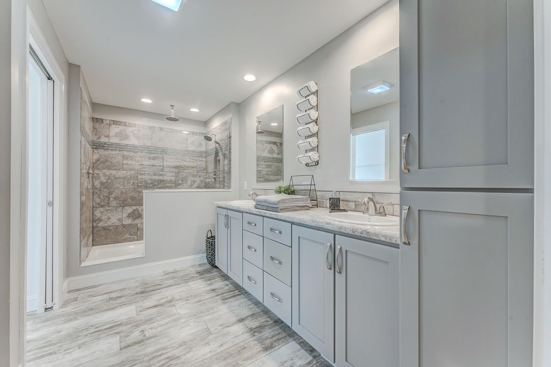 Modern bathroom with light gray cabinets, marble countertop, and wood-style flooring. Spacious shower with stone tiles. Minimalist and serene atmosphere.