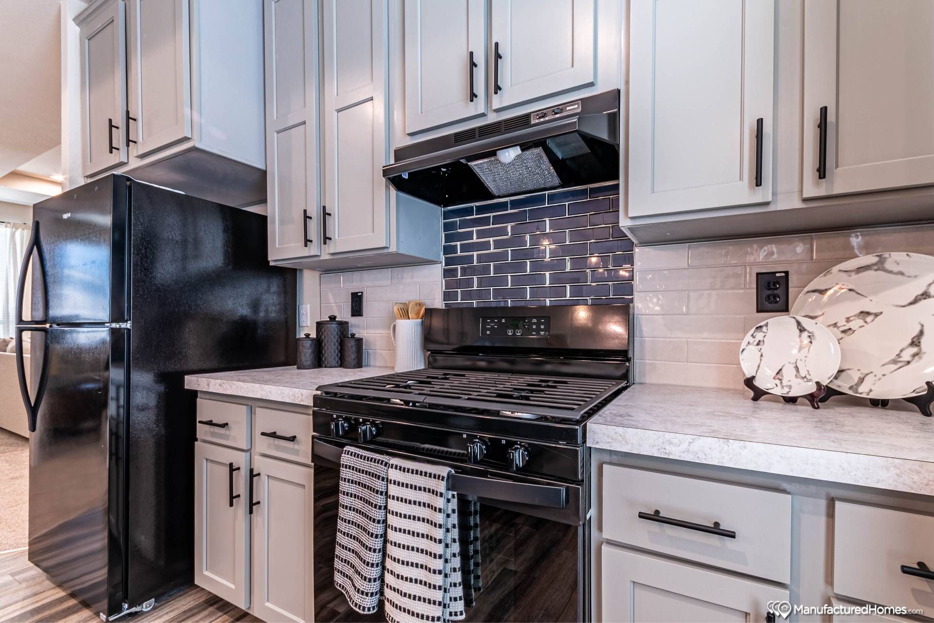 Modern kitchen with black appliances, gray cabinetry, and a sleek black tile backsplash. A striped towel hangs from the oven handle, adding a cozy touch.