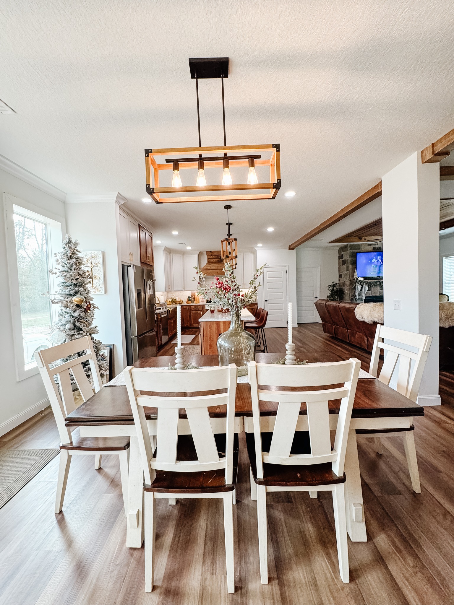 Modern dining room with a rectangular wood table, six white chairs, and a central vase with flowers. Warm lighting from a geometric chandelier above. Cozy and inviting ambiance.