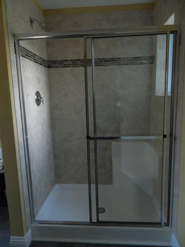 Modern shower with glass doors and silver frame, beige tile walls, and a decorative horizontal strip. The space is clean and minimalistic.