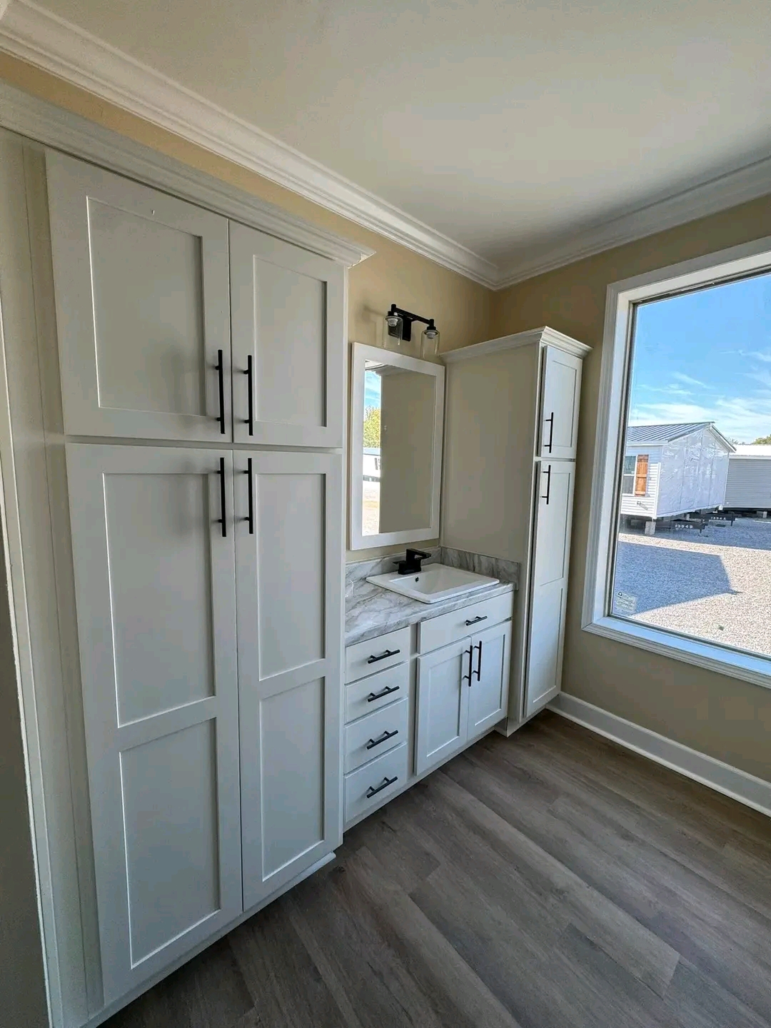 A bright bathroom with white cabinets, a sleek black faucet, and a marble countertop. A large window with a sunny street view enhances the modern feel.