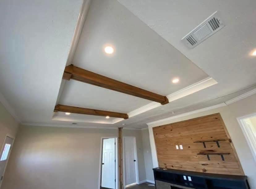 Ceiling view of a modern room with recessed lighting and wooden beams. Clean white walls, a wooden accent wall, and a cozy, minimalist feel.