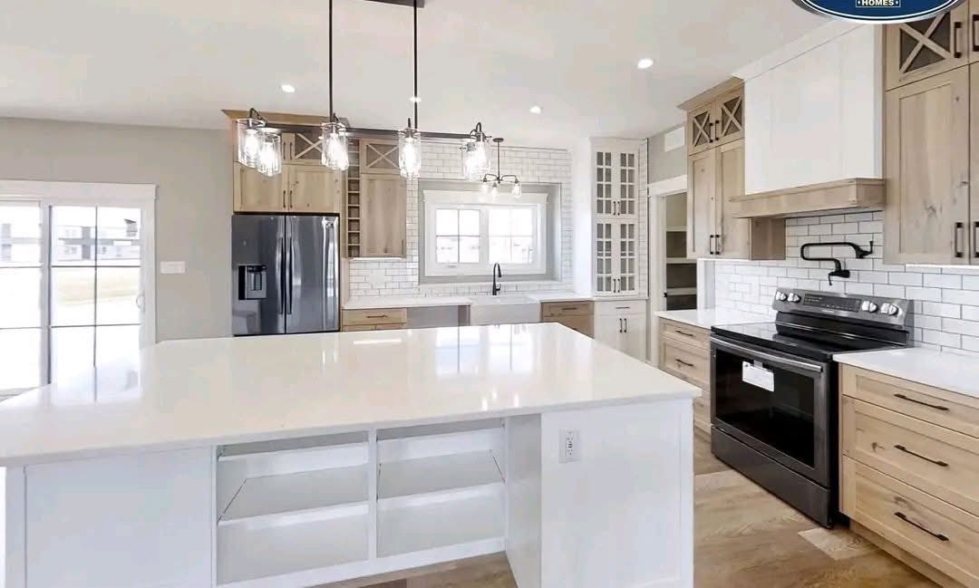 Modern kitchen with a bright, airy feel, featuring a large white island, pendant lights, wooden cabinets, stainless steel appliances, and subway tile backsplash.