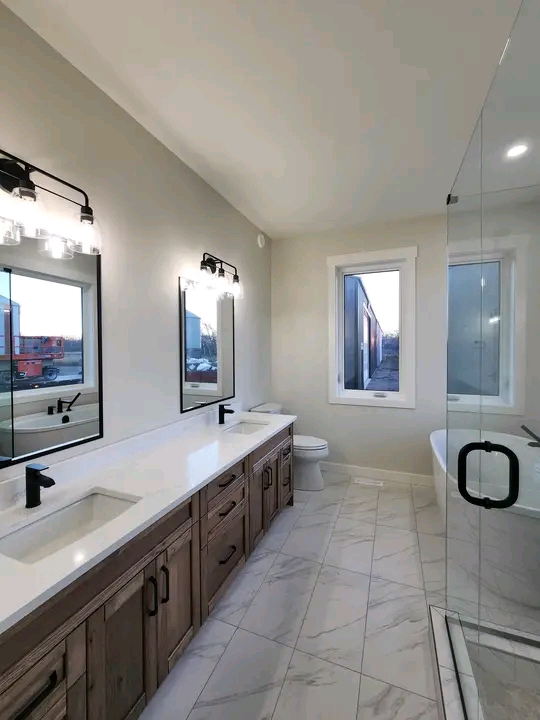 Spacious bathroom with dual sinks, large mirrors, and modern black fixtures. Glass shower and window create an airy, elegant ambiance.