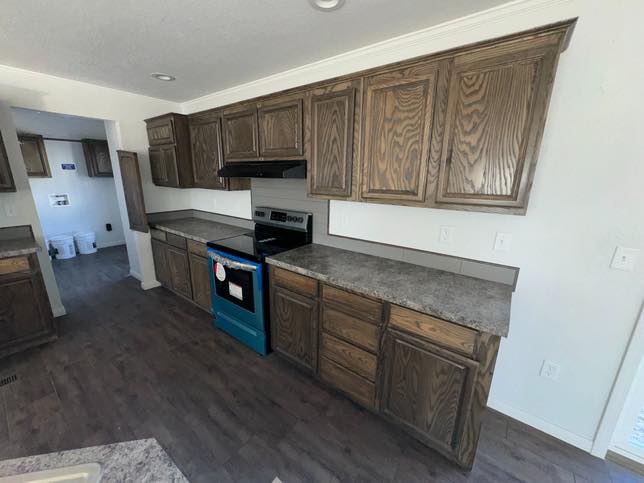Spacious kitchen with dark wood cabinets, marble-like countertops, and a new stainless steel stove. Warm, inviting ambiance with a clean, modern look.