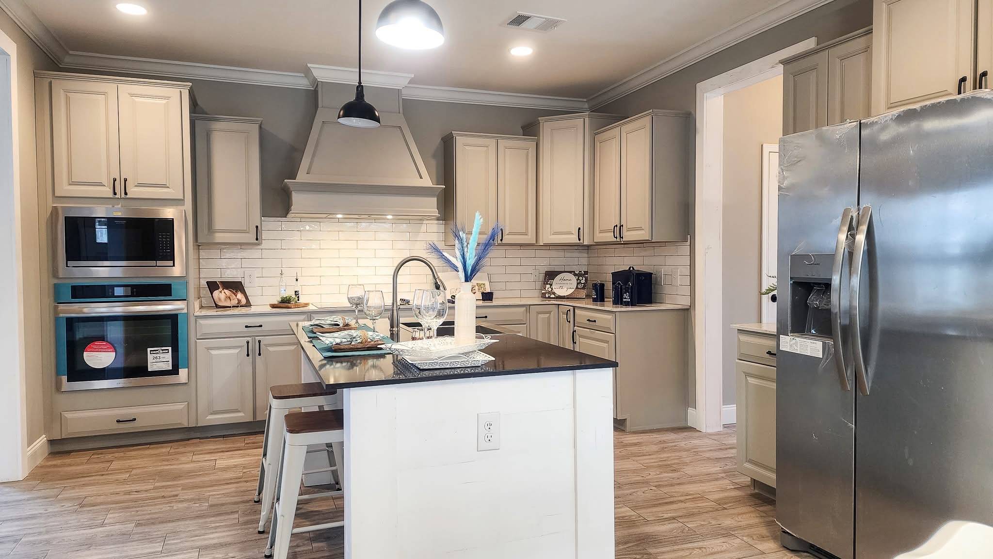 A modern kitchen with beige cabinetry, a sleek island with a black countertop, stainless steel appliances, and wooden flooring. The atmosphere is bright and inviting.