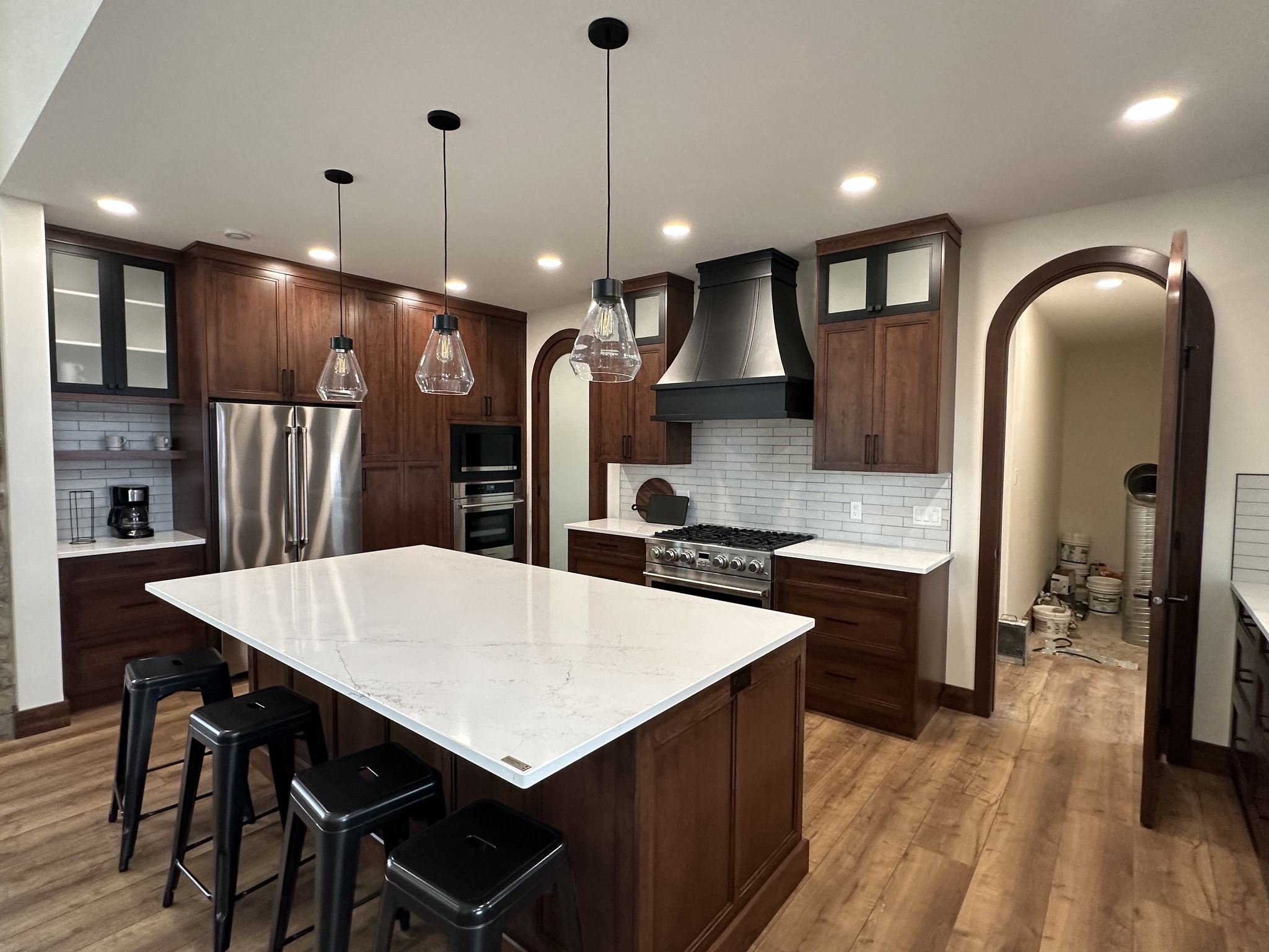 A modern kitchen with rich wooden cabinets, a large white marble island, and three pendant lights. Stainless steel appliances enhance the sleek design.