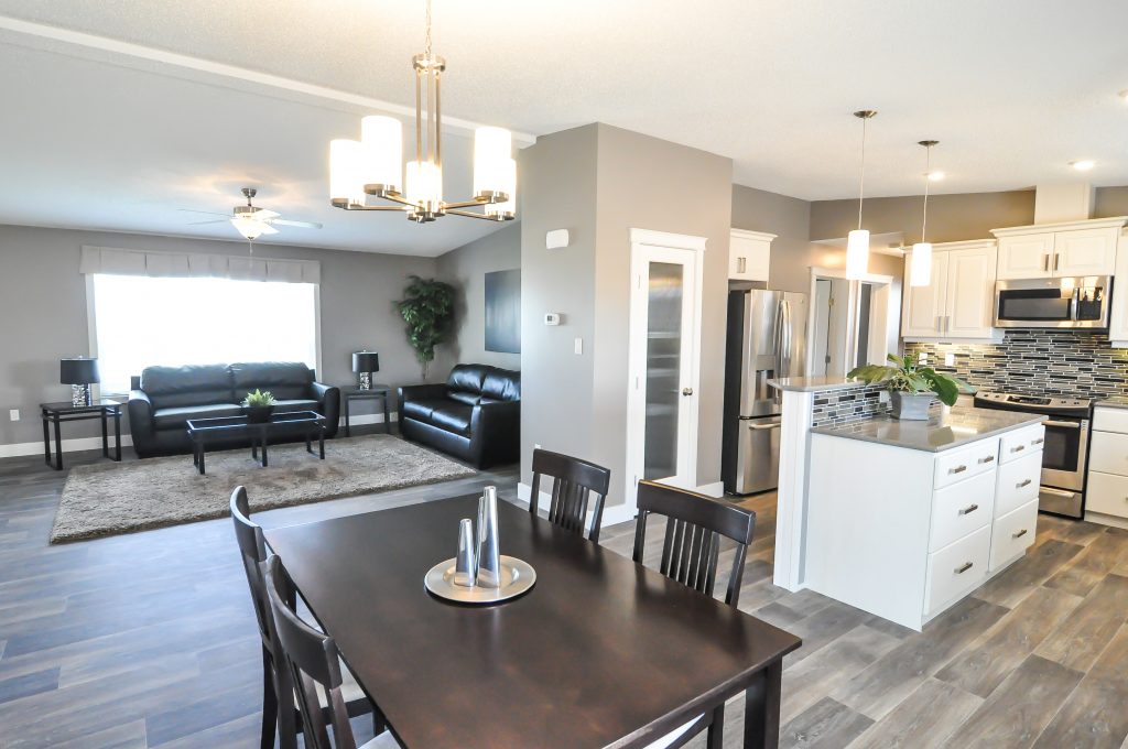 Modern open-concept living space with a sleek kitchen, dining area, and stylish living room. Neutral tones, pendant lights, and leather sofas create a cozy, elegant feel.