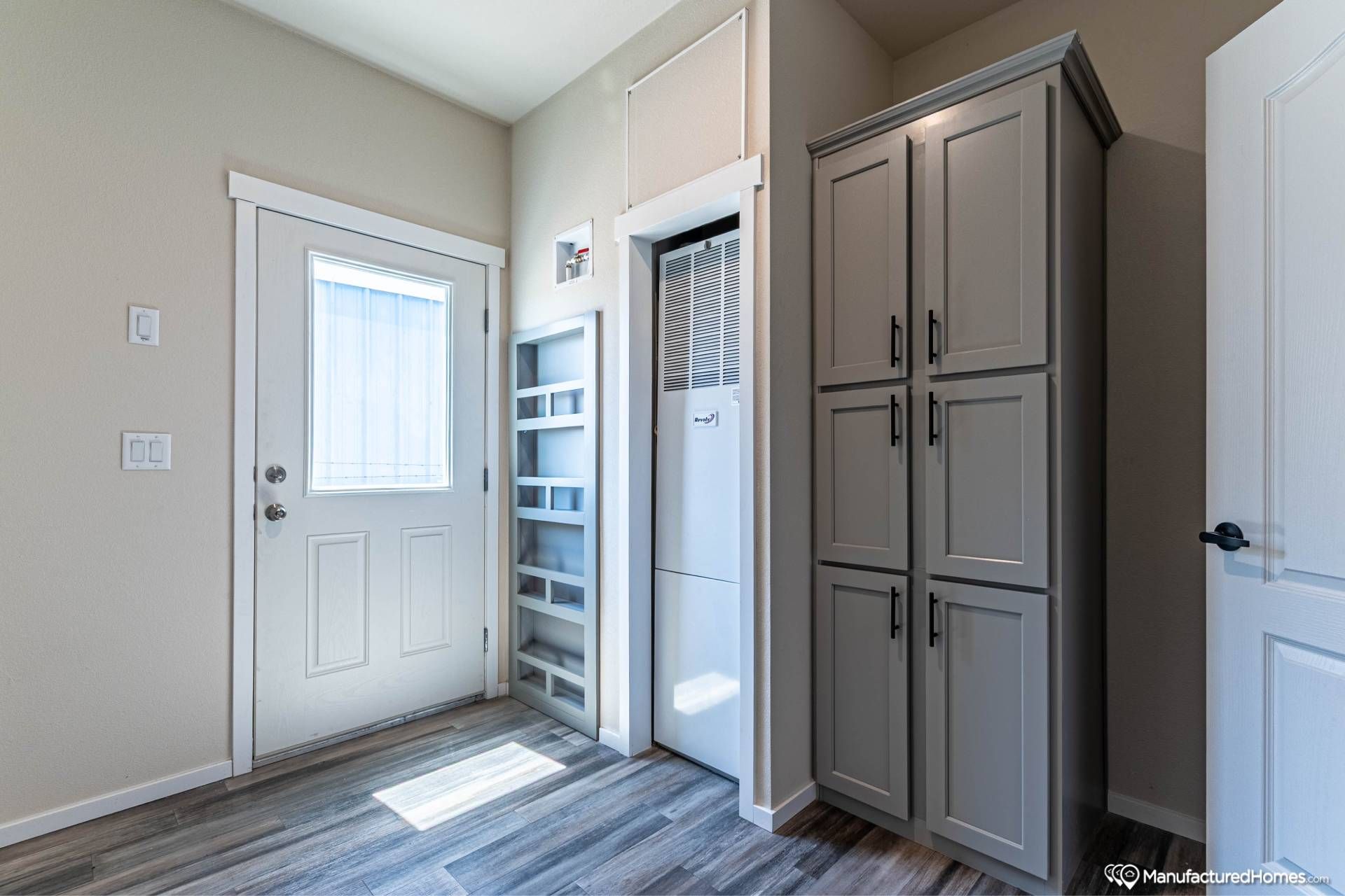 Compact utility room with a door featuring a window, gray cabinets, built-in shelving, and an HVAC unit. Bright, clean, and organized space.