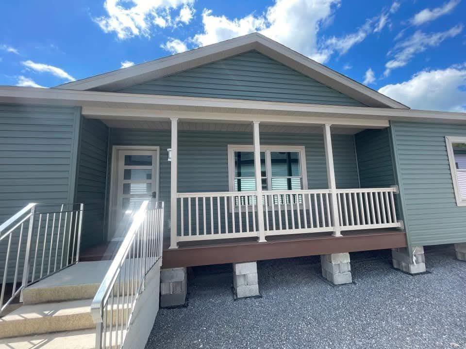 Single-story house with blue siding, white porch railing, and front steps. Bright blue sky with scattered clouds creates a serene atmosphere.
