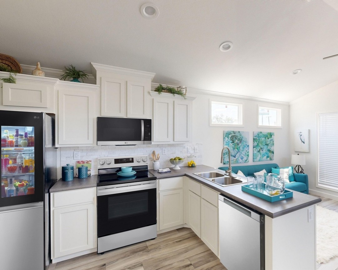 Modern kitchen with white cabinets, stainless steel appliances, and light wood flooring. A vibrant blue couch and artwork add color, creating a cozy feel.