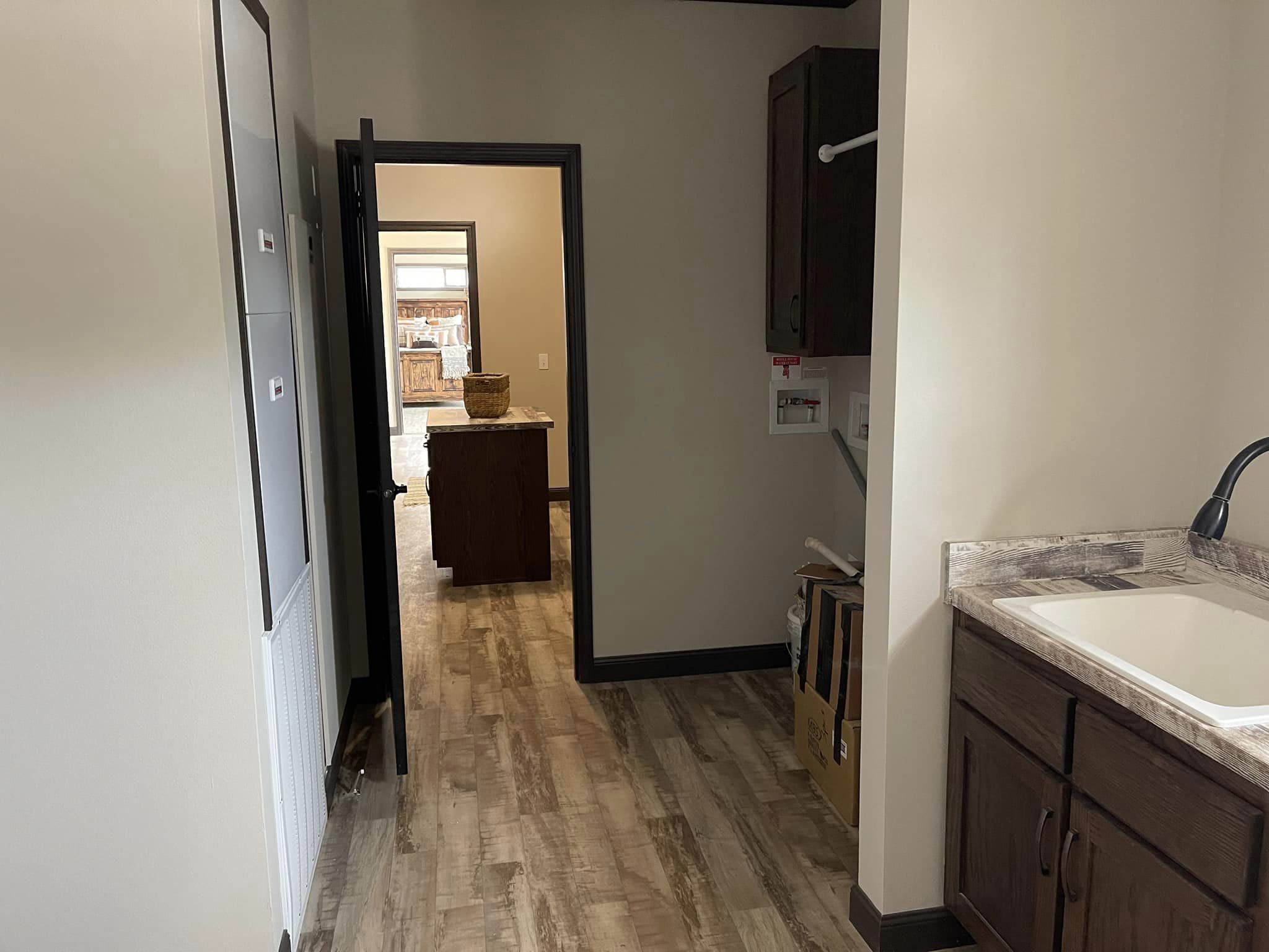 Hallway leads to a kitchen area with wood flooring and dark cabinetry. A countertop with a wicker basket is visible through the open door, evoking a cozy, warm tone.