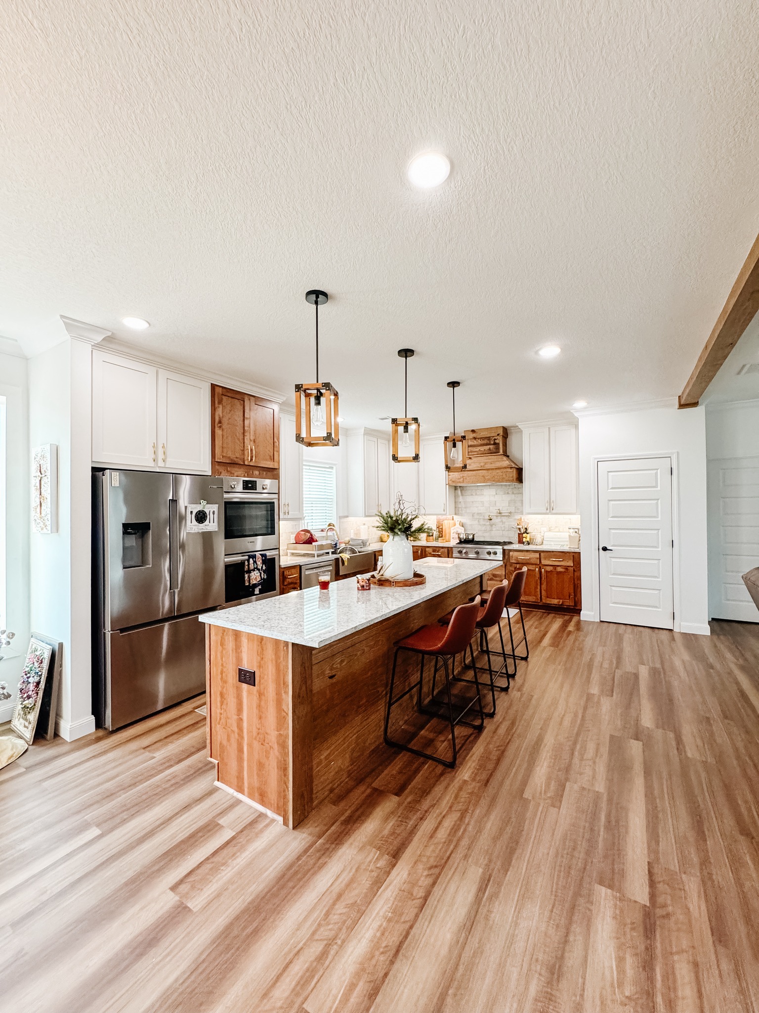 Spacious kitchen with wood floors, marble island, and four orange chairs. Modern appliances set against white and wood cabinets. Bright and inviting.