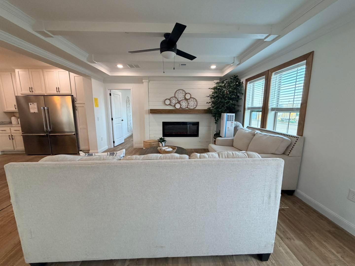 Modern living room with beige sectional sofa facing a shiplap fireplace, decorated with circular wall art. Natural light streams through large windows.