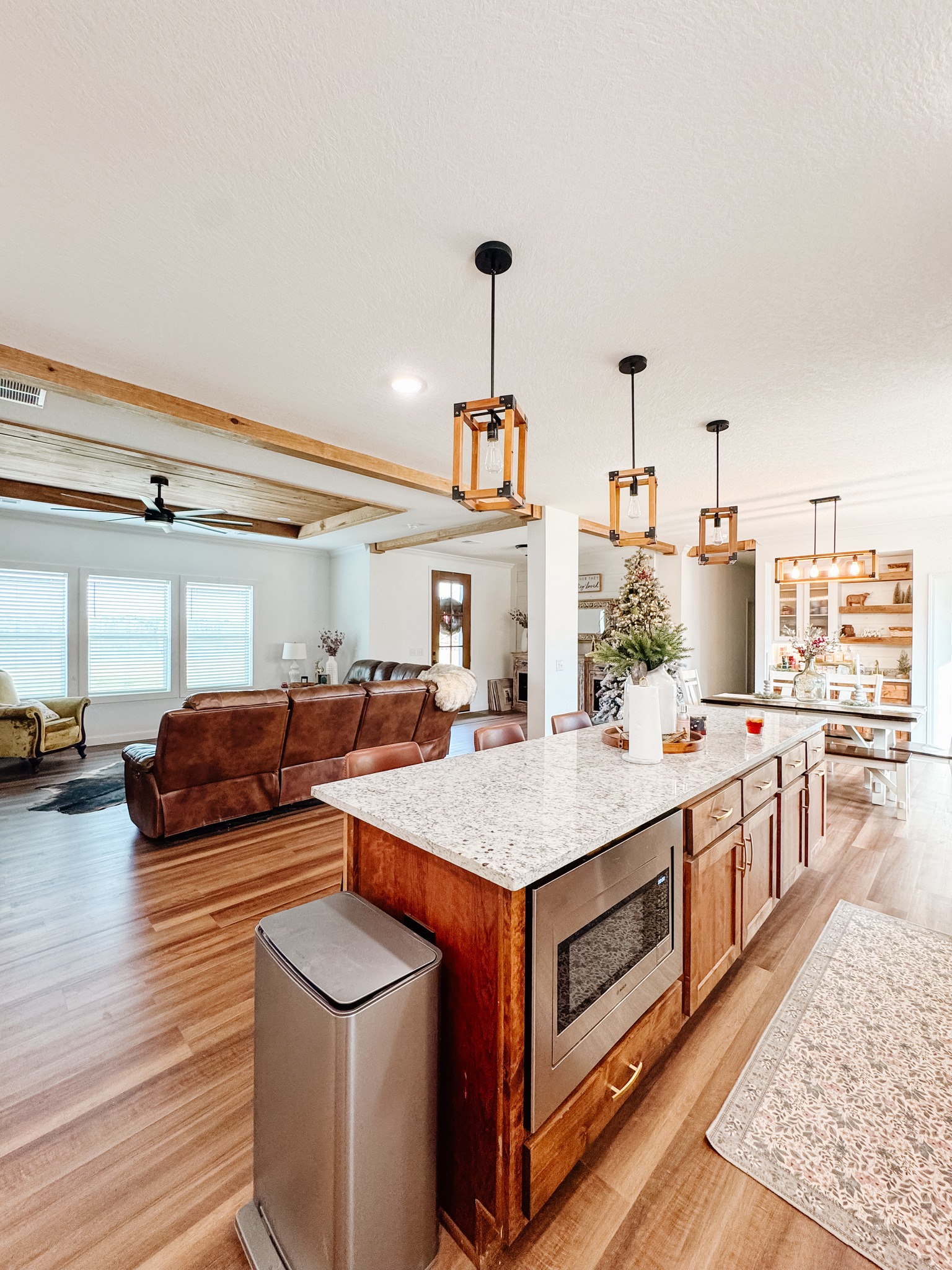 Spacious open-plan kitchen and living area with modern pendant lights and wood beam ceiling. Cozy seating and Christmas decorations create a warm, inviting atmosphere.