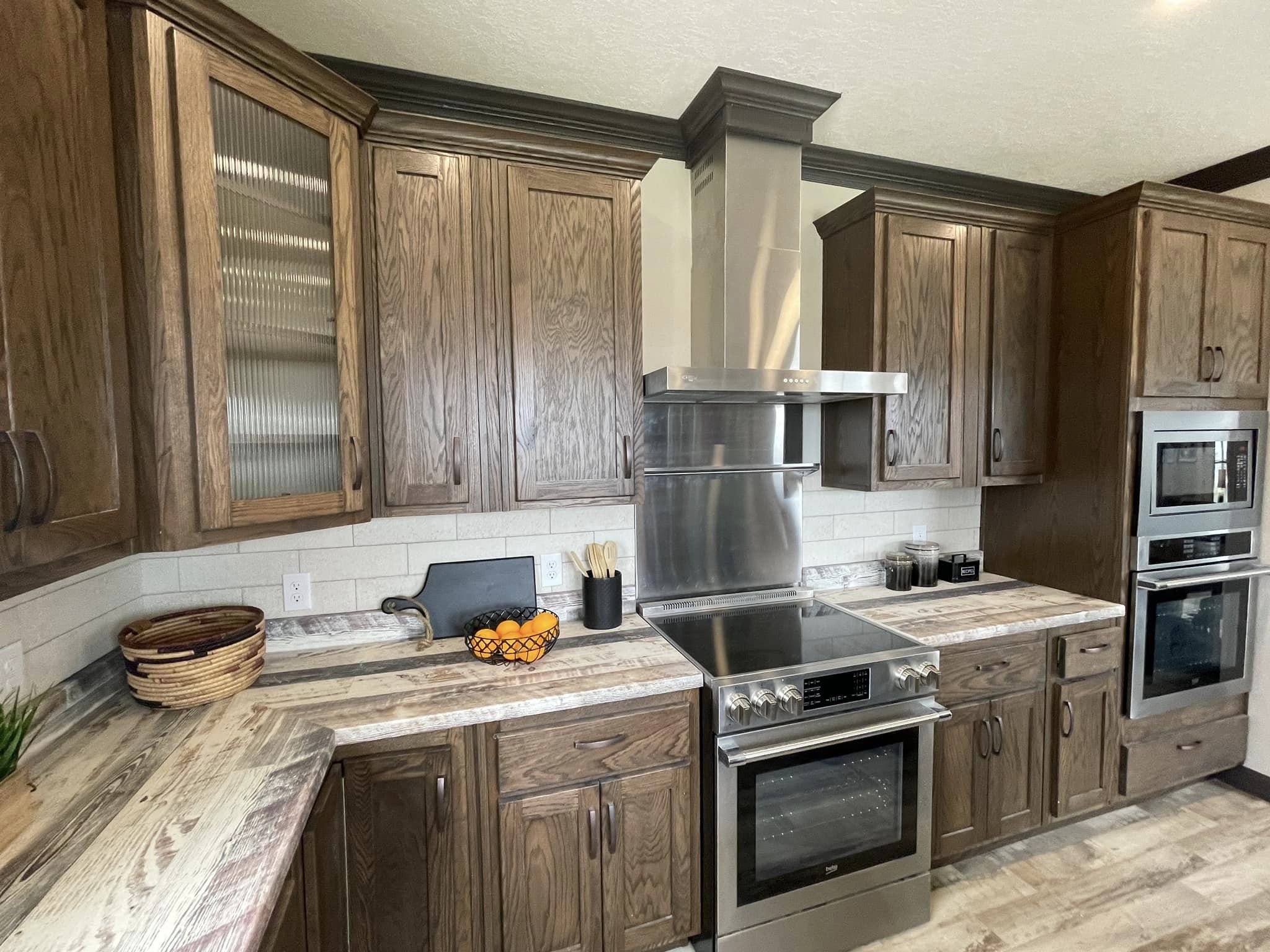 Rustic kitchen featuring dark wood cabinets, stainless steel stove with hood, and a natural wood countertop. A bowl of oranges adds a pop of color.
