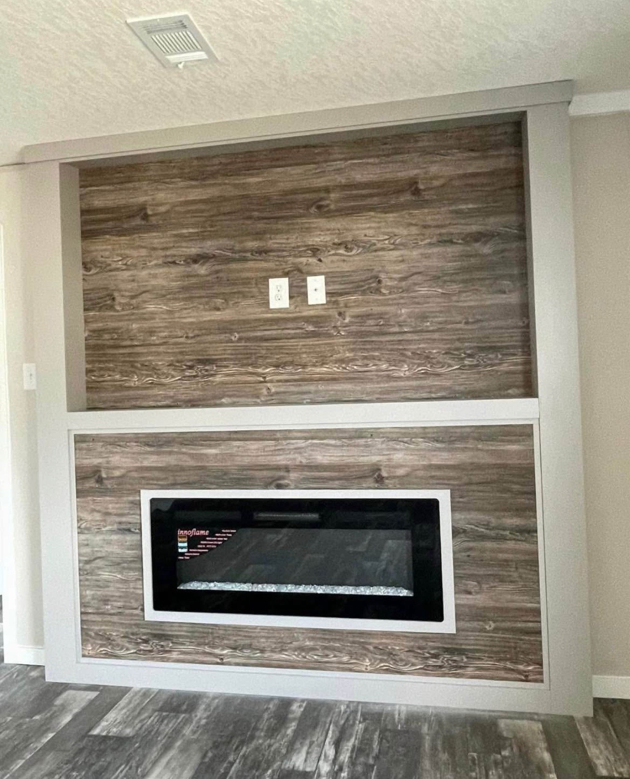 Modern electric fireplace set in a rustic, wood-paneled wall with sleek gray trim. The room has a calm, contemporary feel.