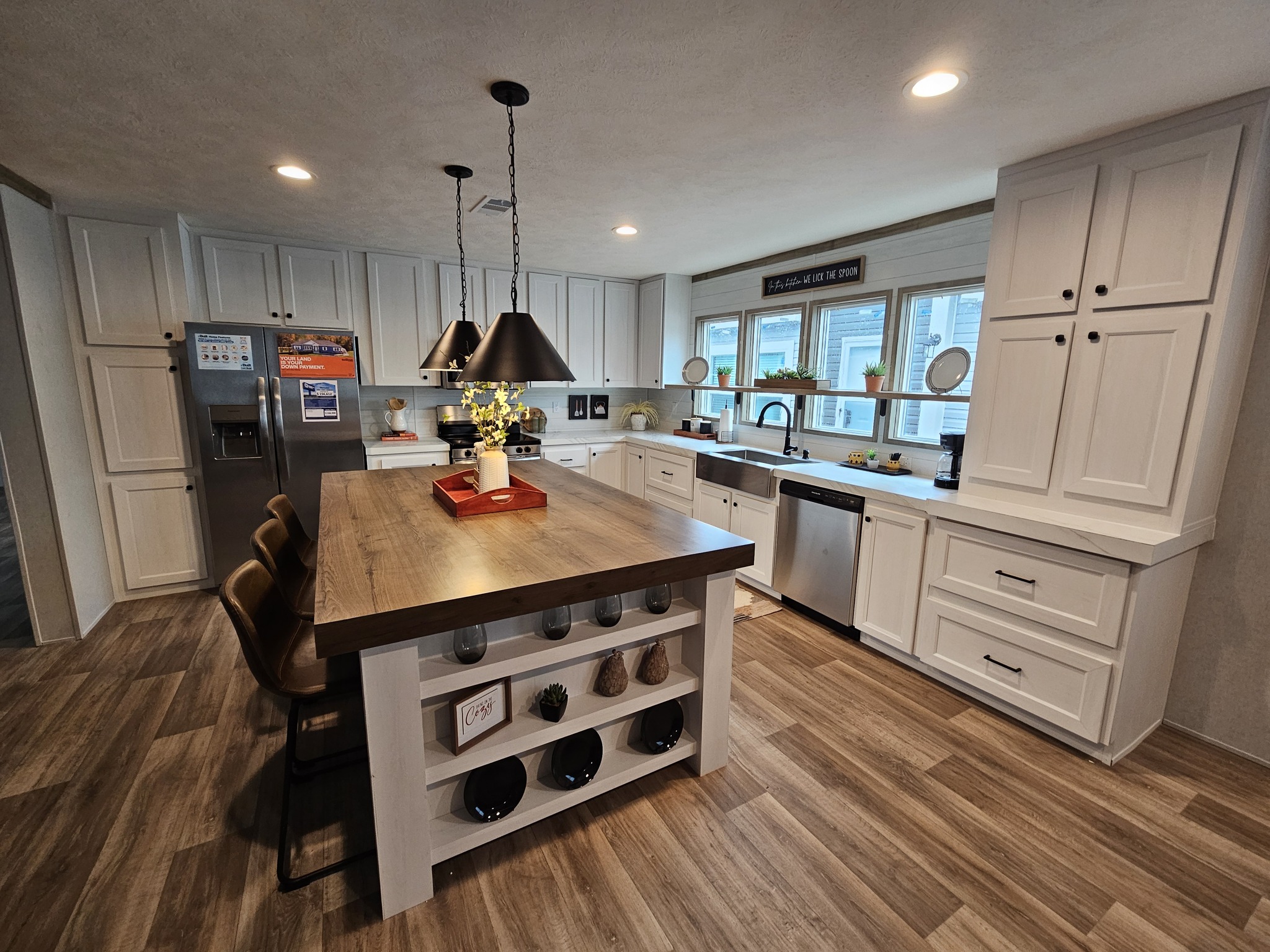 Modern kitchen with a large wood island, surrounded by white cabinets and stainless steel appliances. Bright overhead lights create a cozy atmosphere.
