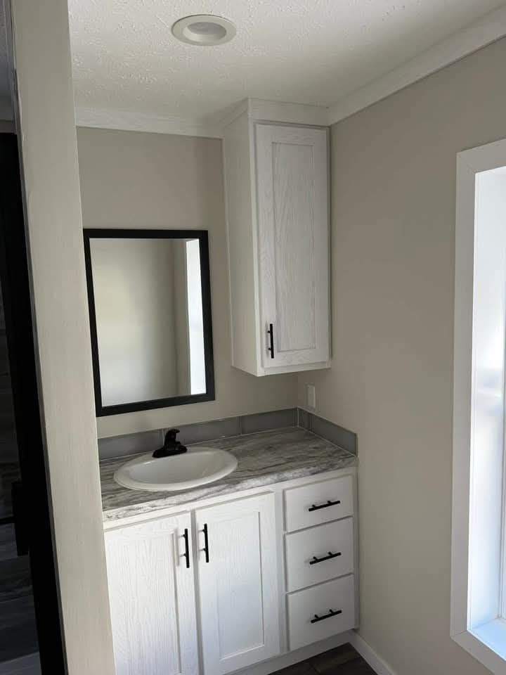 Small bathroom with a marble-top vanity, white cabinets, black hardware, a round basin, and a rectangular mirror. Bright and modern feel.