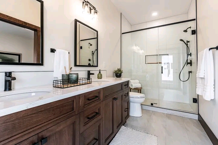 A modern bathroom with a double-sink wooden vanity, black framed mirrors, and a glass-enclosed shower. Neutral tones and sleek fixtures create a serene atmosphere.