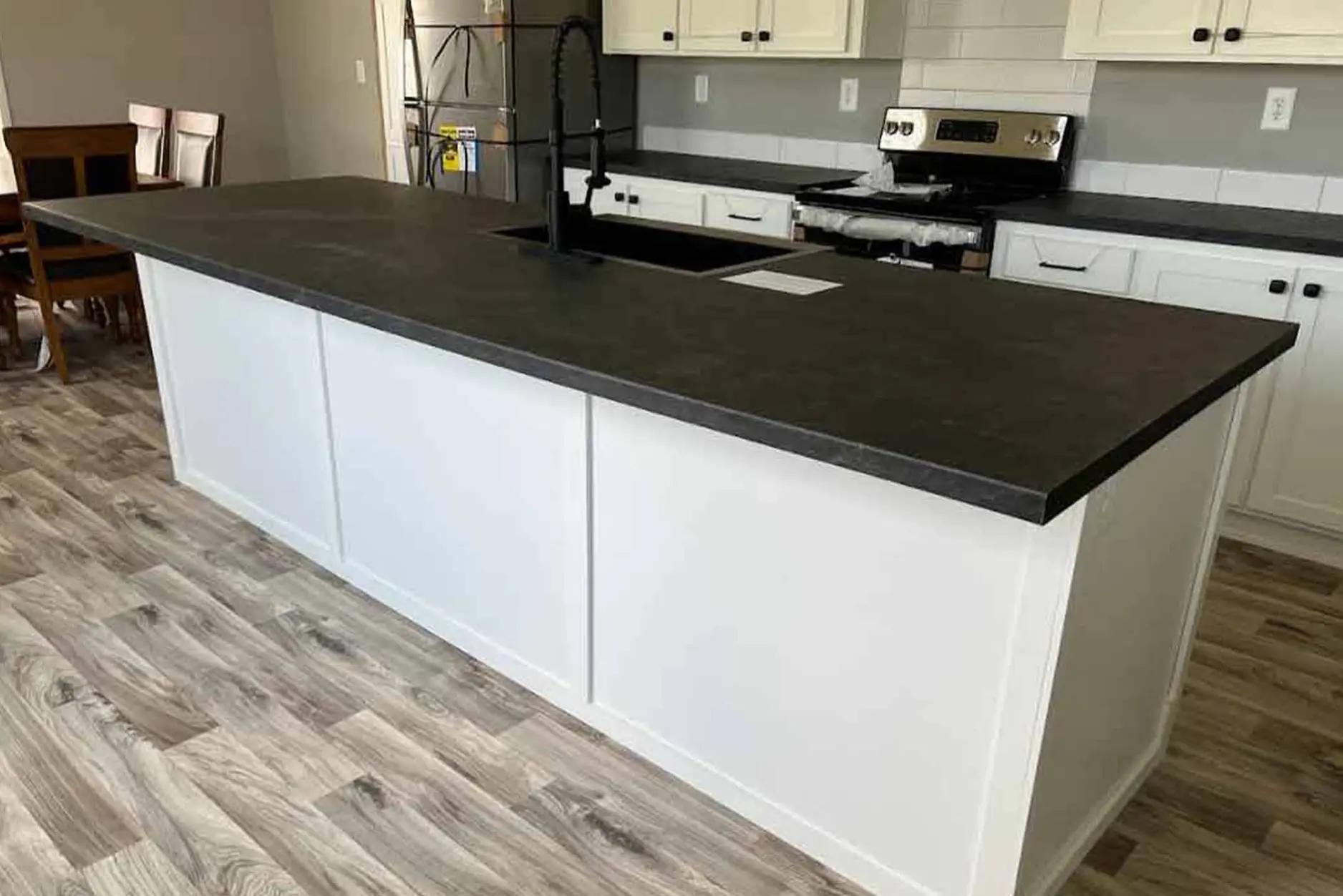 Modern kitchen with a large white island featuring a dark countertop and black faucet. Light wood flooring and white cabinets create a clean, airy feel.