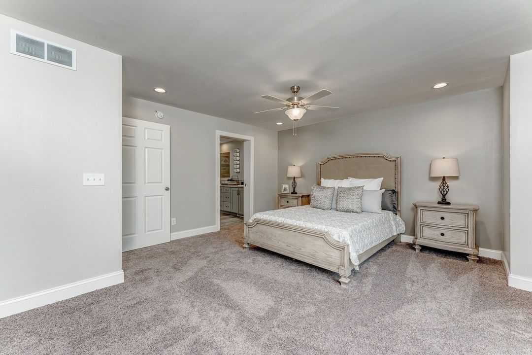Spacious bedroom with neutral tones, featuring a large bed with gray upholstered headboard, matching nightstands, and soft lighting, creating a calm ambiance.