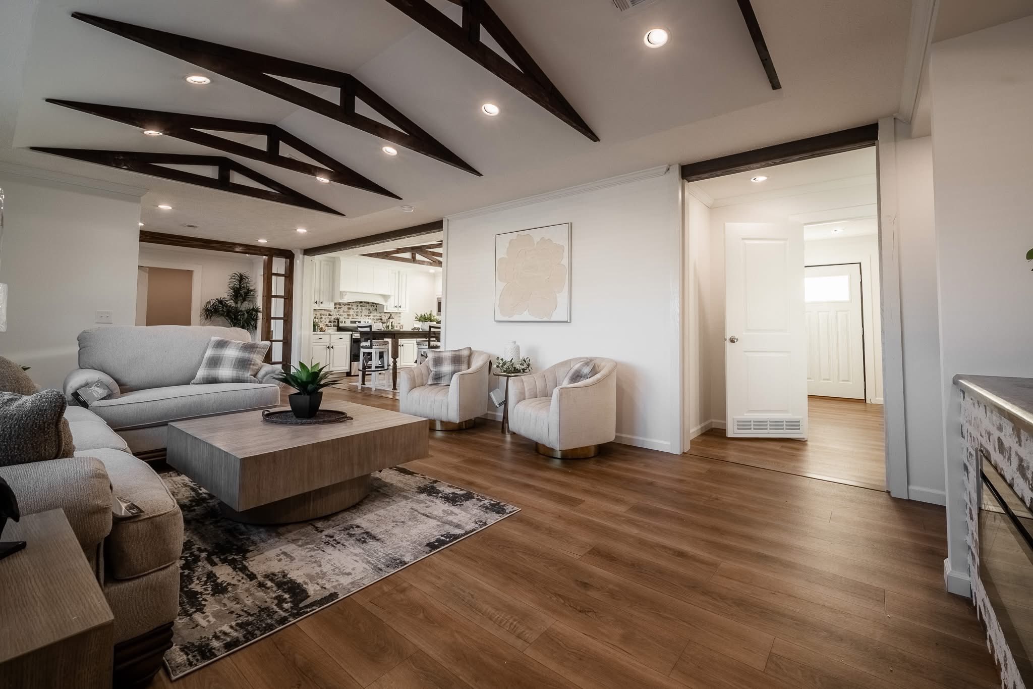 Spacious living room with modern decor. Features include a large gray sofa, wooden coffee table on a patterned rug, and exposed ceiling beams. Cozy, inviting ambiance.