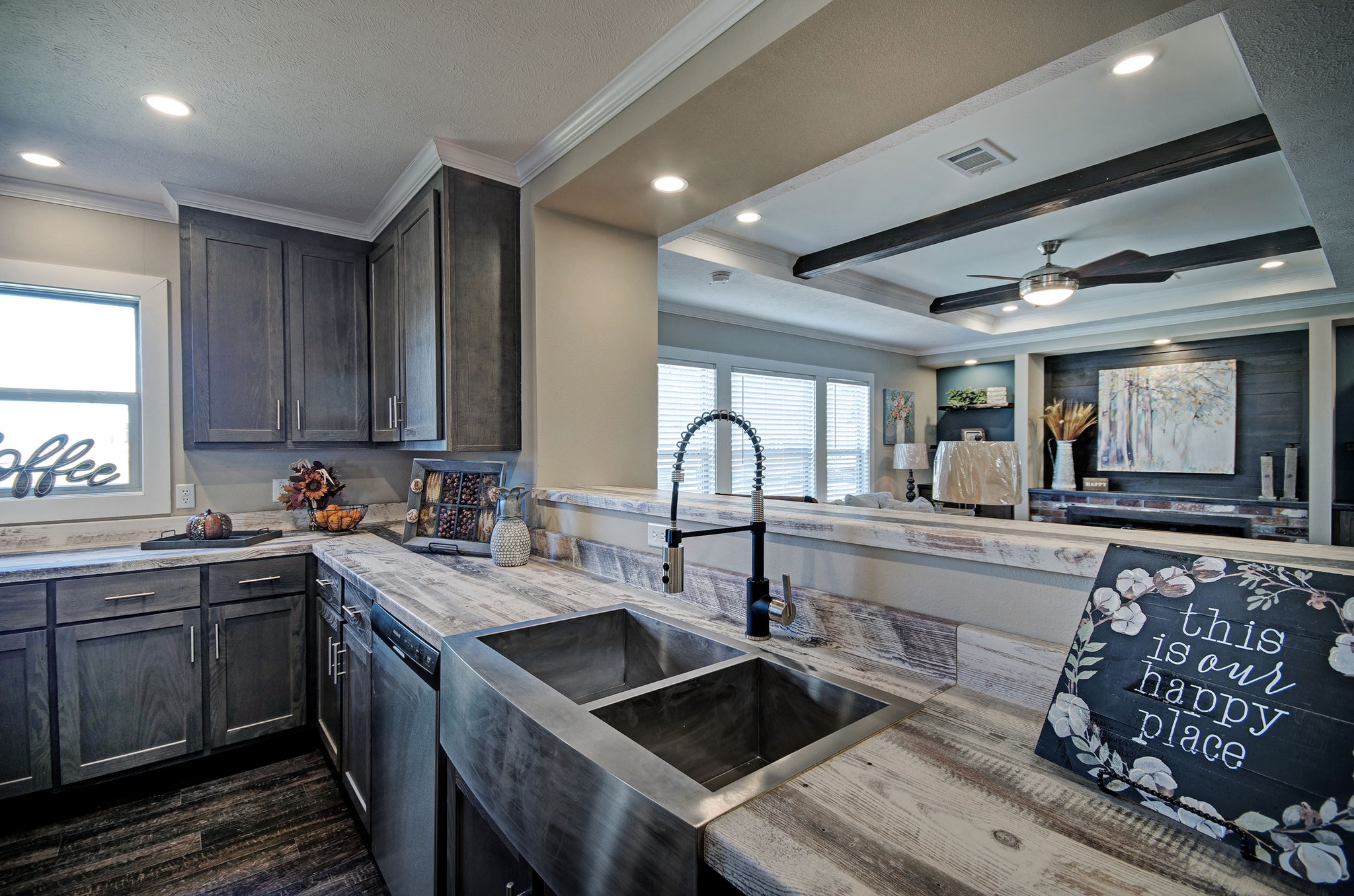 Modern kitchen with dark wood cabinets, marble countertops, and a stainless steel sink. A sign reads "this is our happy place," conveying warmth.