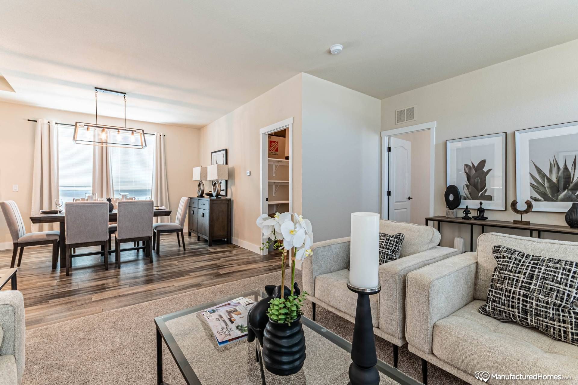 Modern living and dining area with neutral tones. Beige sofas, a black coffee table, and flower decor; dining table with chairs under a chic light fixture.