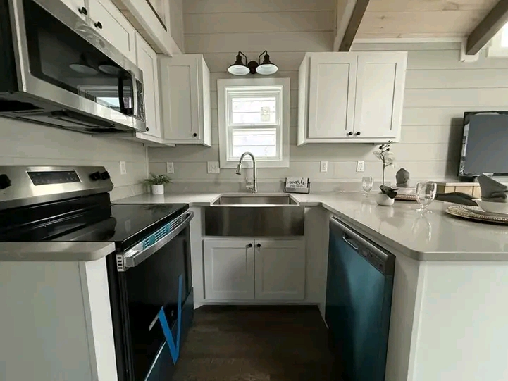 Modern kitchen with white cabinets and stainless steel appliances, including a farmhouse sink. Natural light filters through a window above the sink.