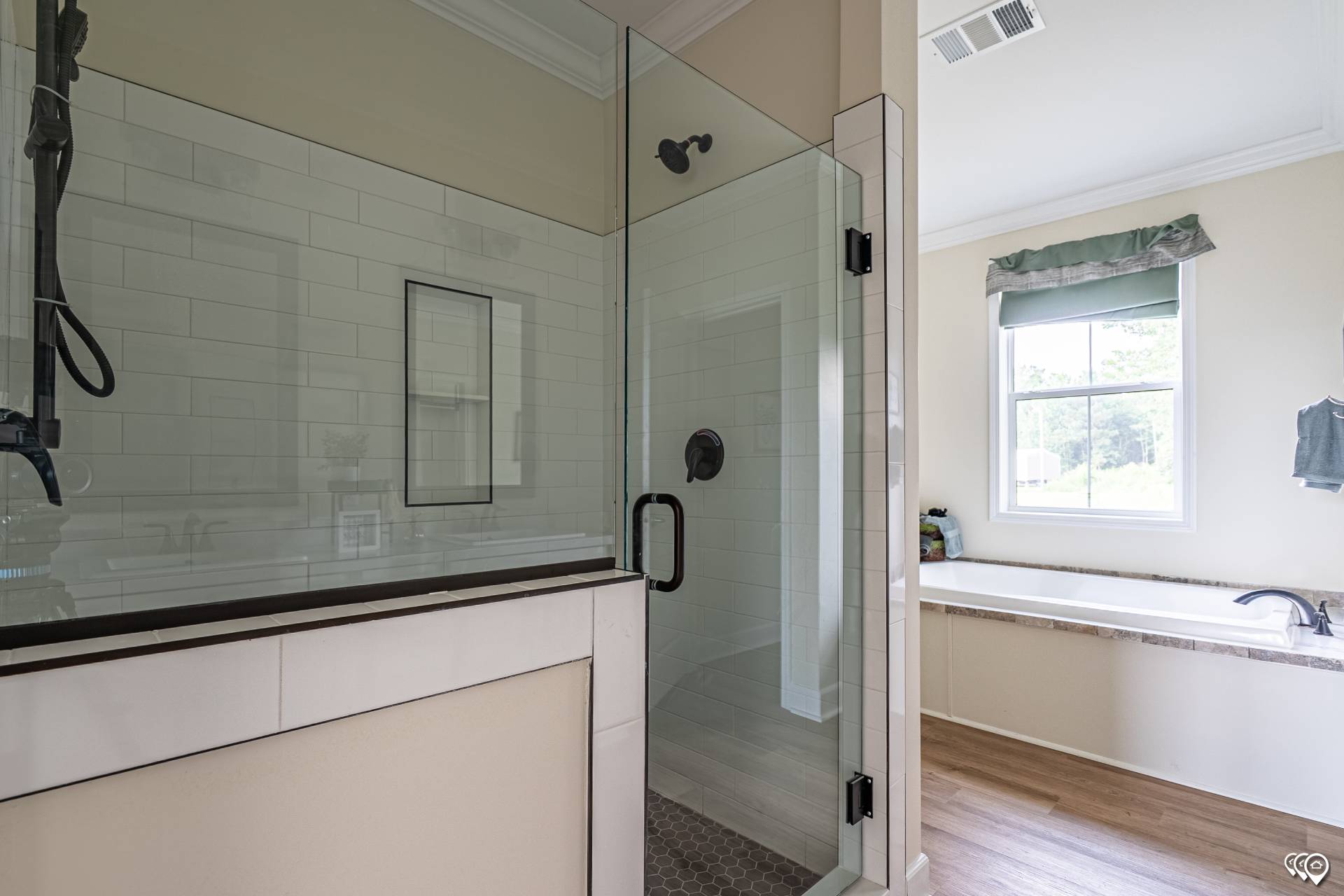 Bright bathroom with glass-enclosed shower featuring white subway tiles, adjacent to a bathtub with a large window, light wood floor, and soft neutral tones.